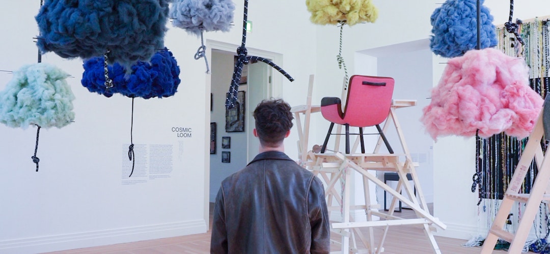 A young man stands in the middle of an art exhibition featuring colourful clouds hanging from the ceiling