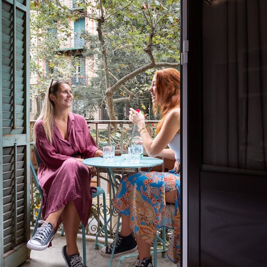 A bright picture of two girls sitting on a blue table on the balcony 