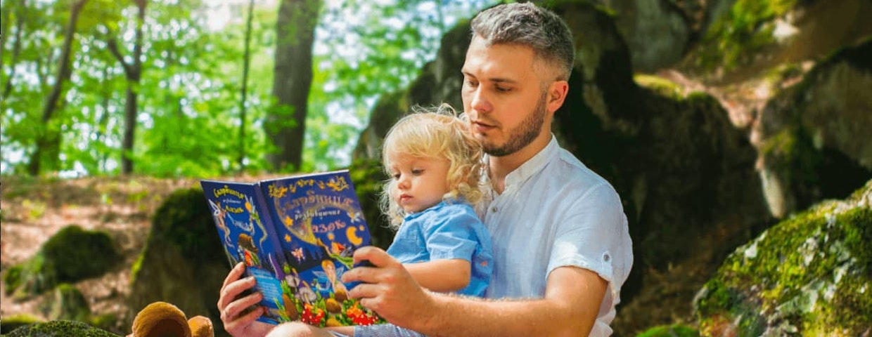 Barn och pappa har högläsning i skogen