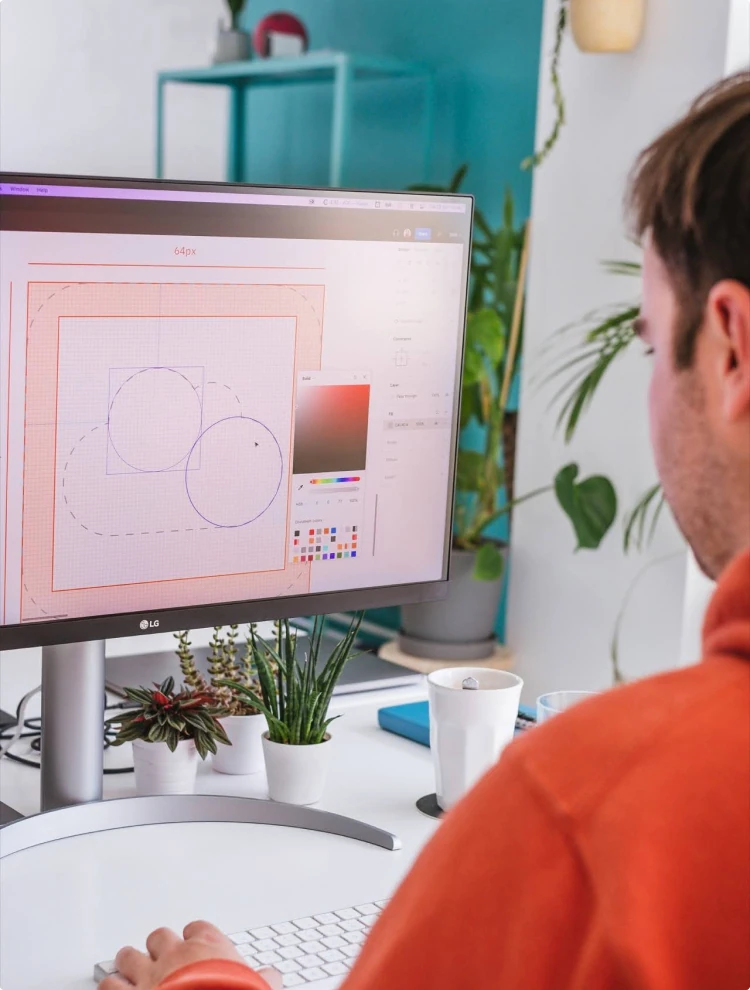 designer looking at monitor as they're working on an icon in a design tool with an office wall in yummygum's brand color turquoise in the background with some plants