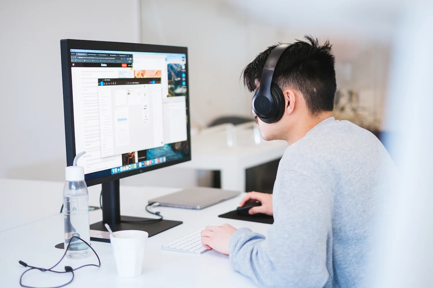 Former intern UX Design intern Duy sitting at desk while slightly bent over and wearing headphones. In the picture he is seen from the rear-side as he's looking intensely at his monitor