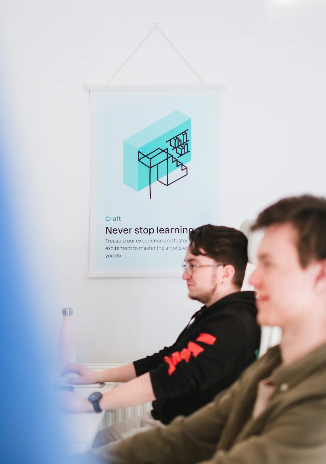 Two Yummygum employes as seen from the side out of focus with a wall mounted poster in focus in the center of the photo that shows an illustration of a library with stairs and some text explaining the illustration