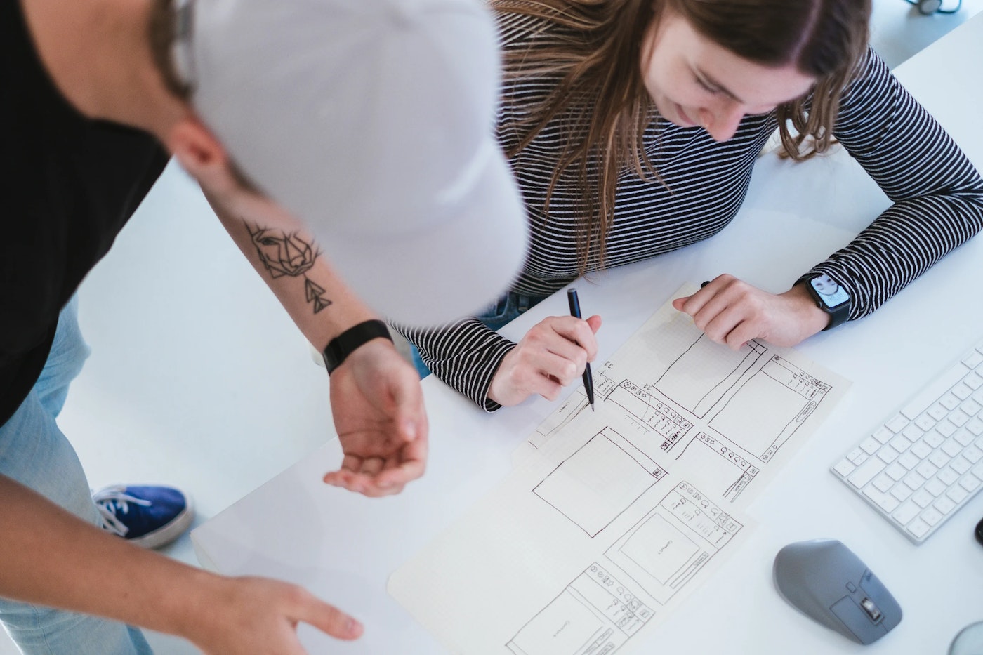 Two people hunched over looking at and discussing wireframe sketches as one of the persons holds a pen