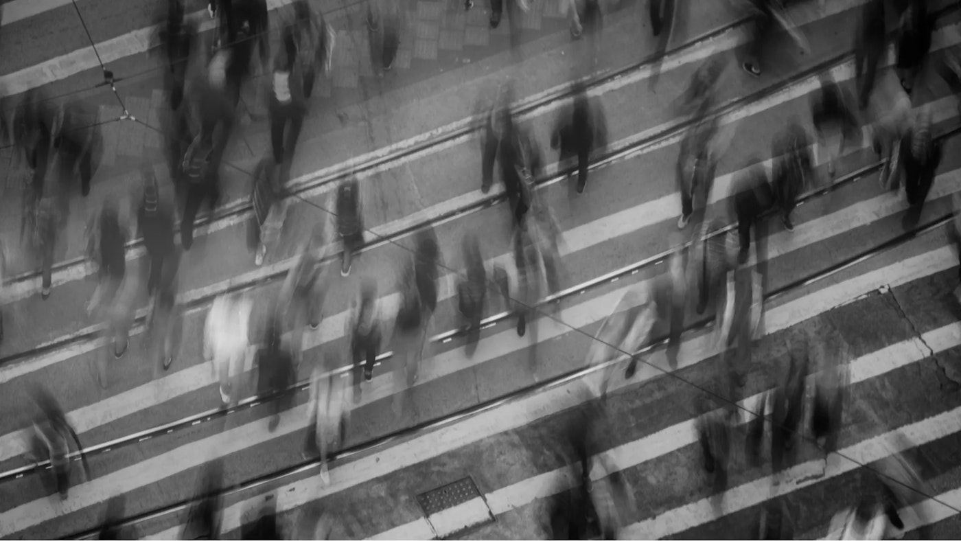 Black and white top down long exposure view of pedestrians crossing a street.