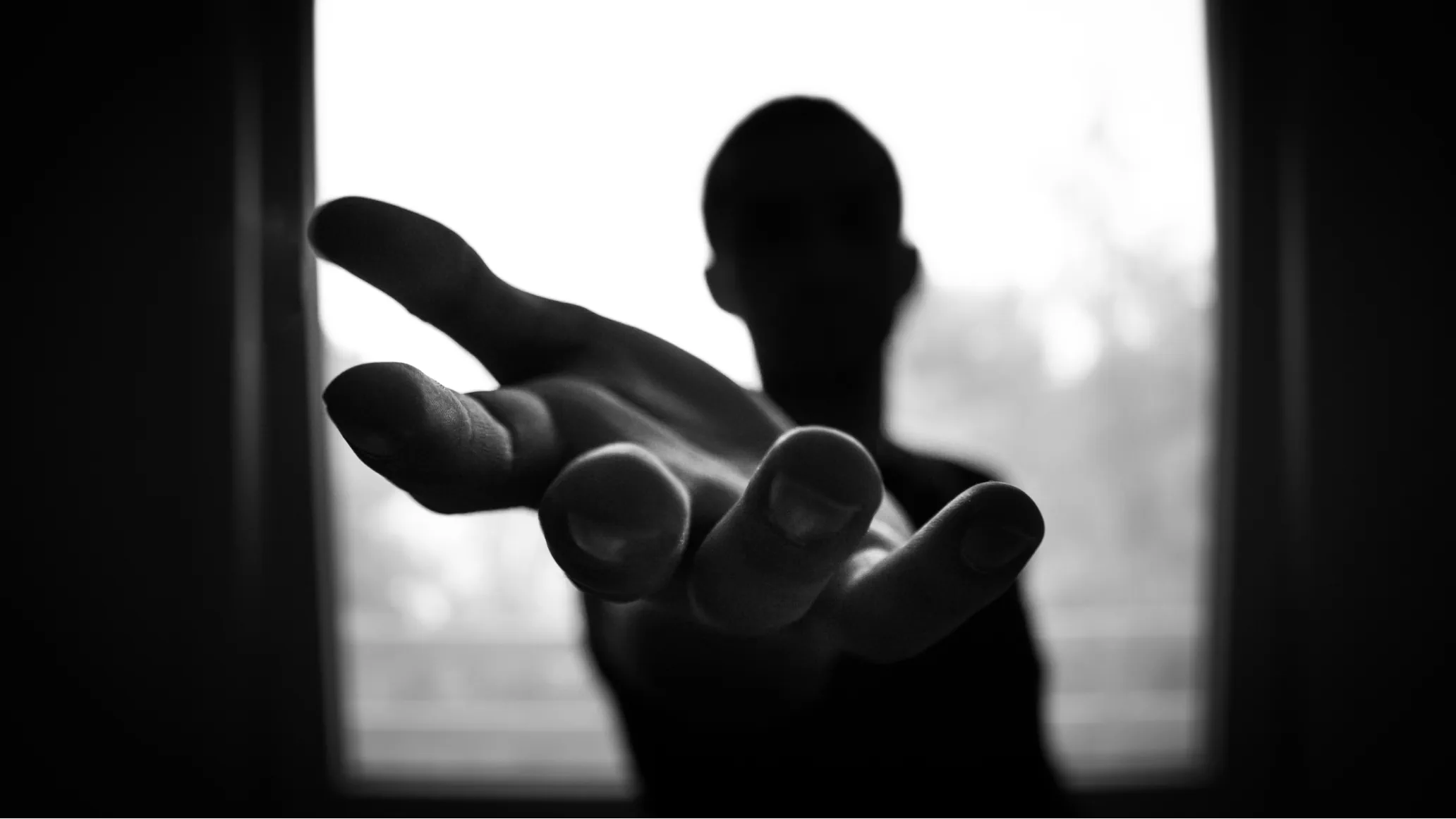 Black and white photo of unrecognizable person reaching out their hand to the camera.