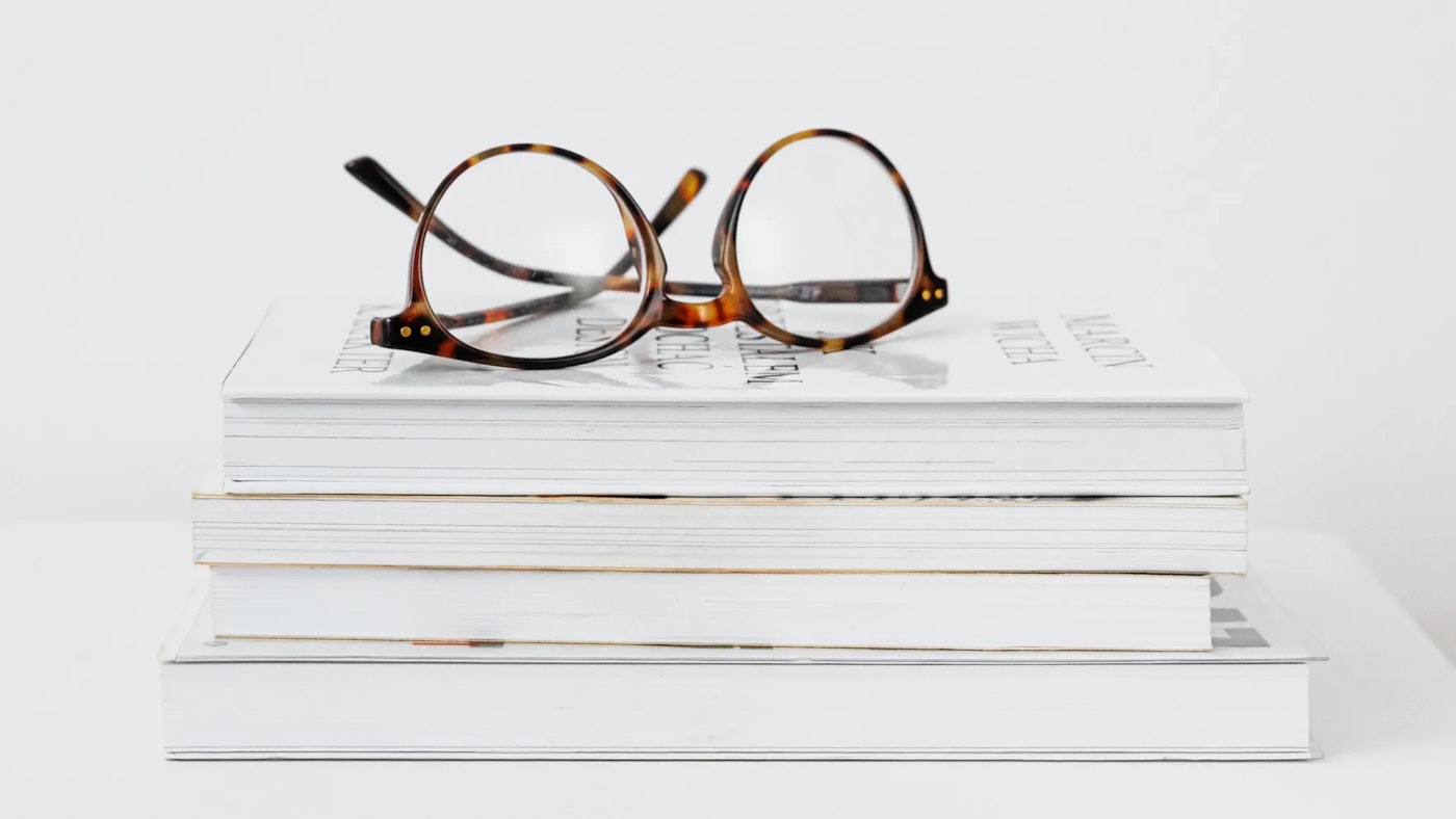 Spectacles upside down on a pile of four books in a serene white setting..