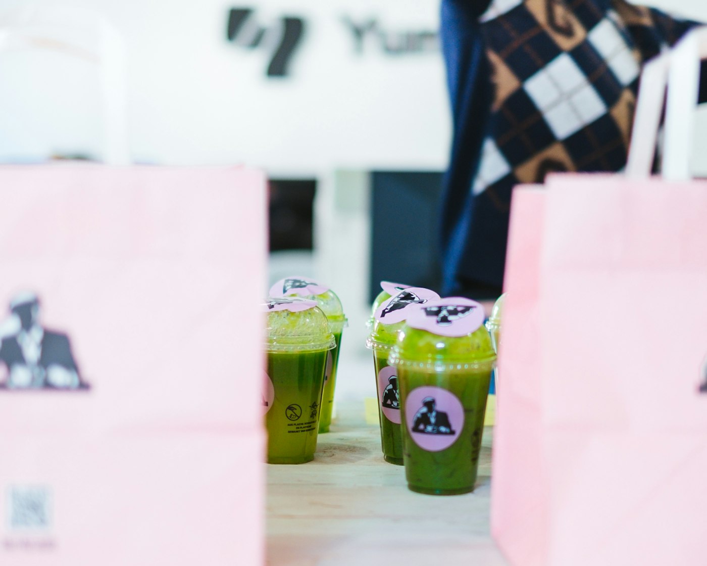 Plastic cups with a plant based green smoothie in them, in between two pink paper bags