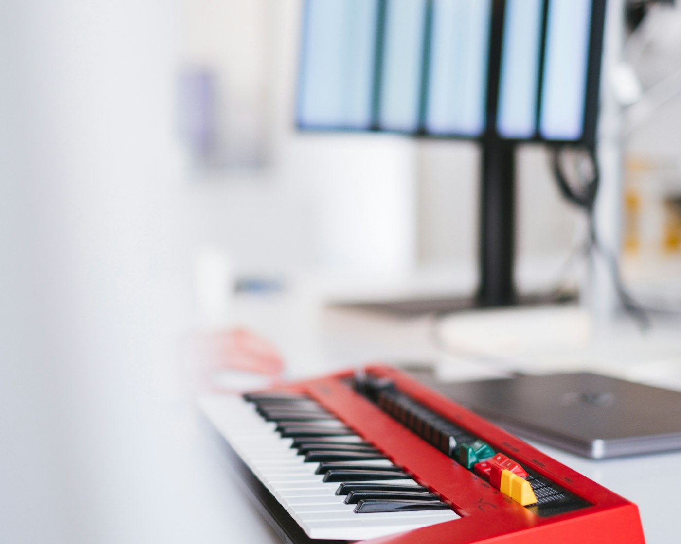 Synthesizer with red casing in focus on a desk in the white Yummygum office. Just out of focus is a closed laptop and a display.