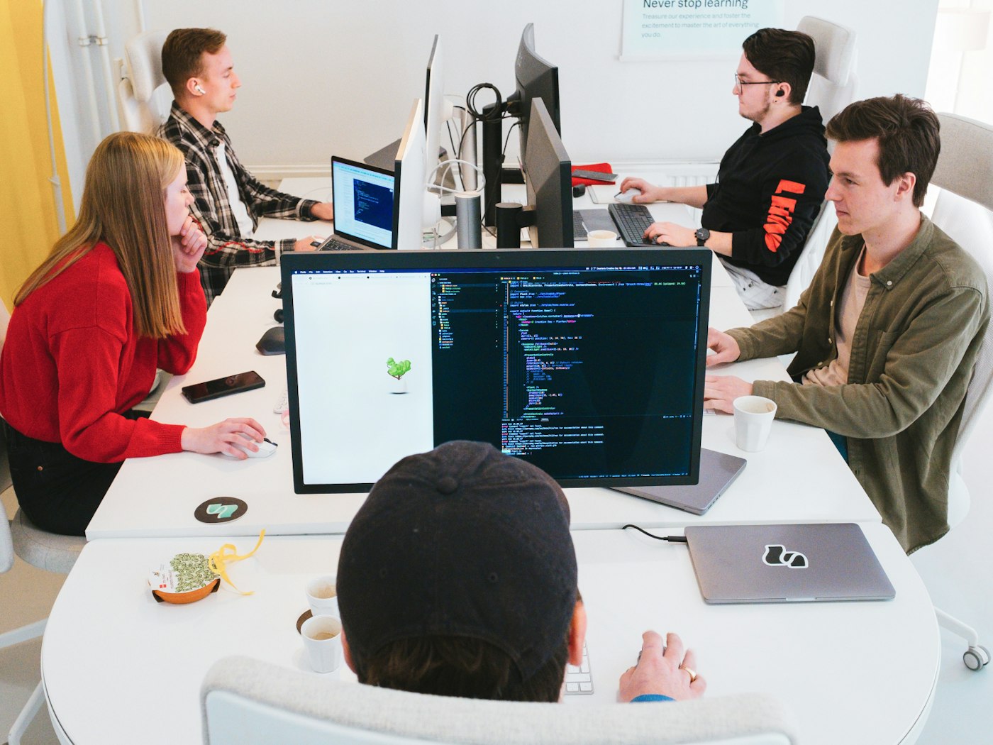 A group of people all sitting behind their desk while working and looking at their displays. The front most display shows a code editor.