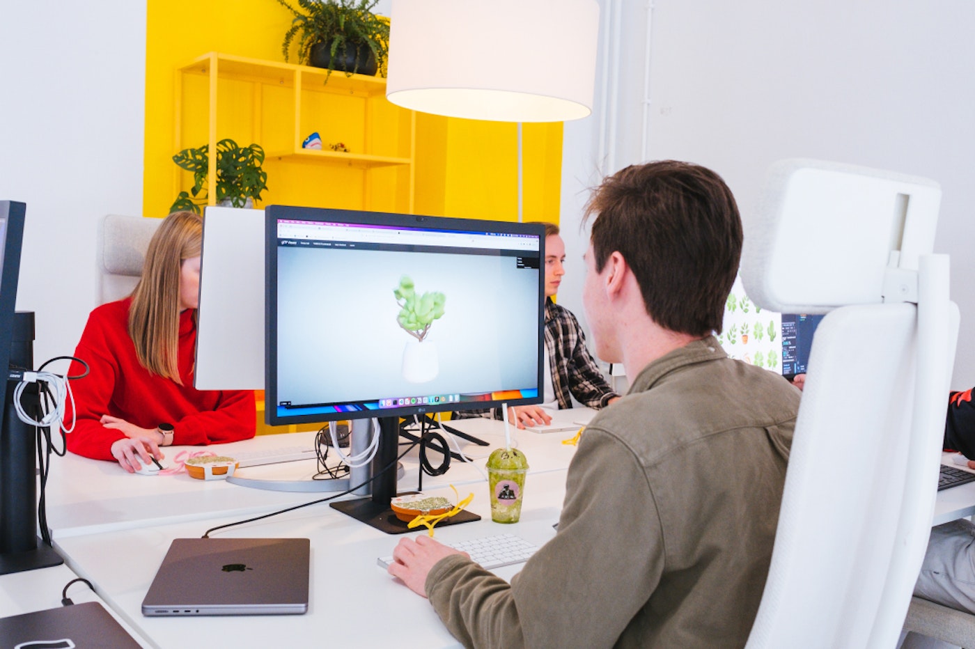 Person working on a closed laptop with an external display. The display shows a 3d model of a plant.