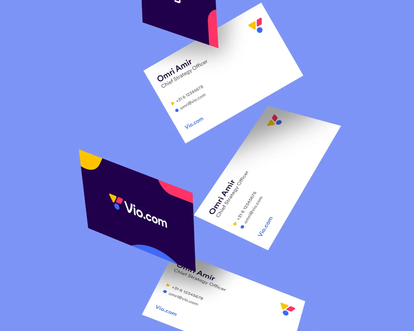 Five business cards playfully shown, looking like they are falling down. The business cards contrast with the light blue background behind the cards. Some of the business cards show a side that is dark blue side. In the middle of the dark blue background is a white logotype that says Vio.com. The logotype is accompanied by a logo mark consisting of three colored shapes. The other business cards show details of a person amongst which their name, email and phone number.