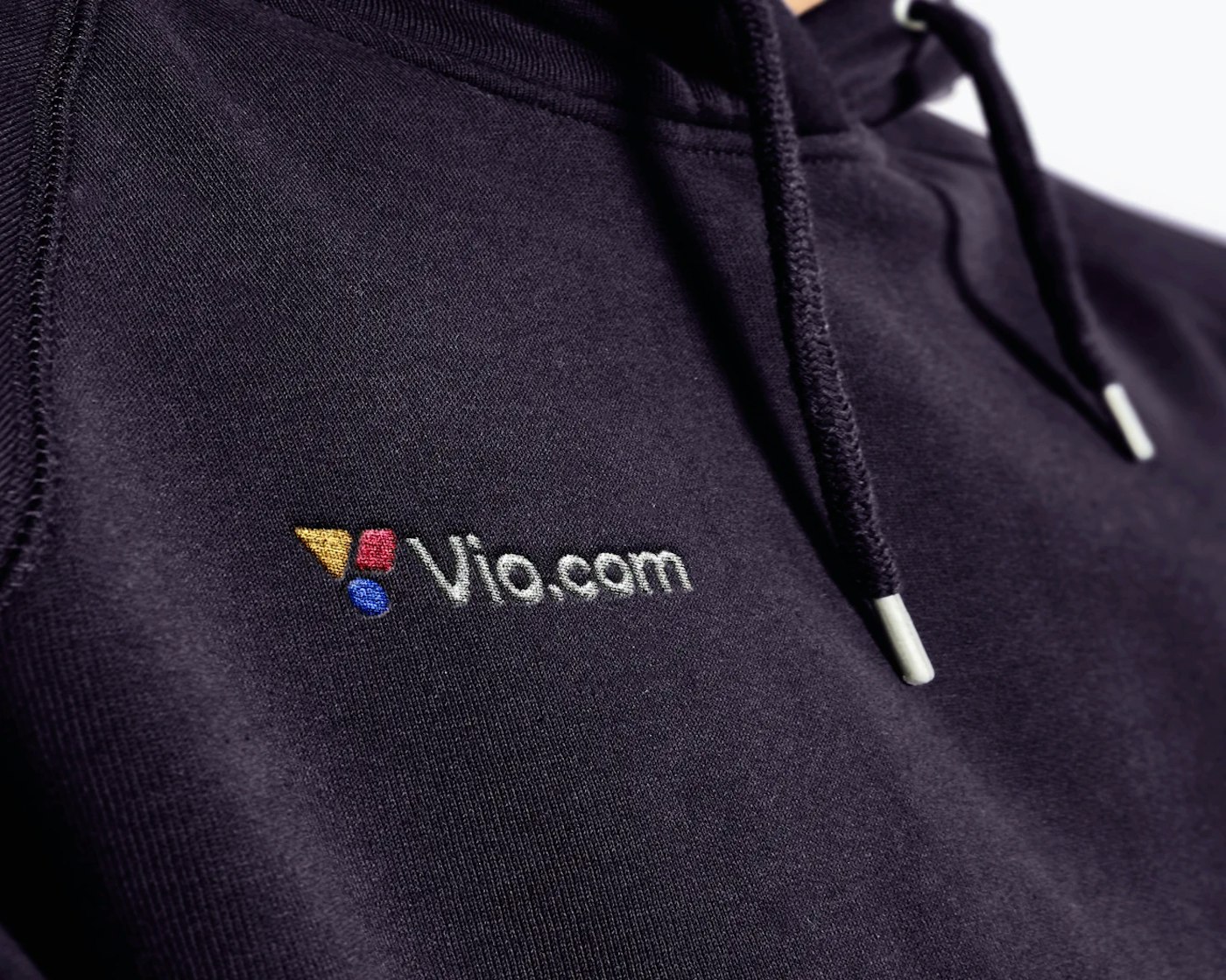 Perspective close up of a dark blue hoodie with an embroidered Vio.com logo with a white logotype combined with a white logo mark consisting of three colored shapes.