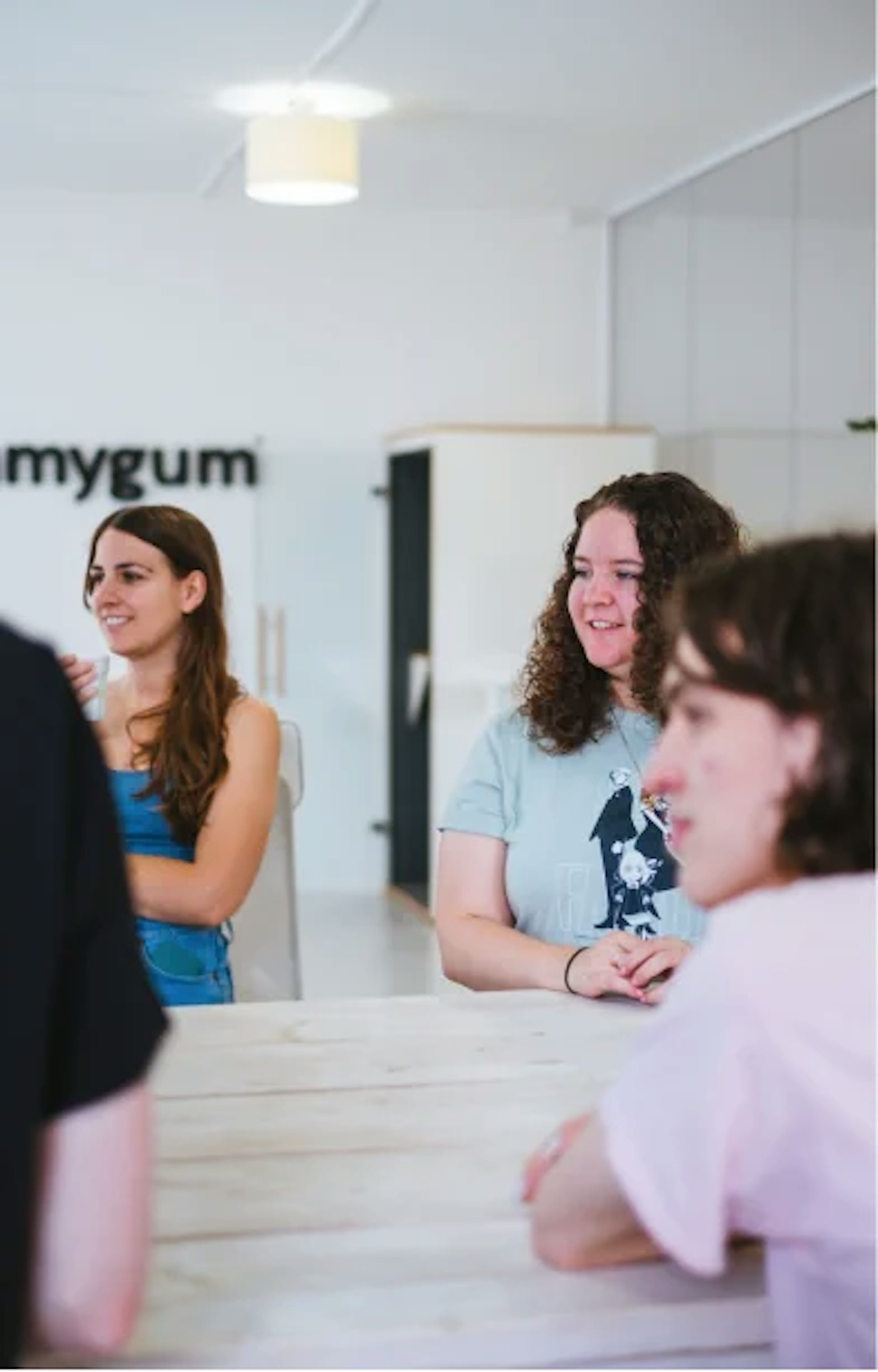 People standing and sitting around a table, all three looking towards the left, at something that is out of frame.