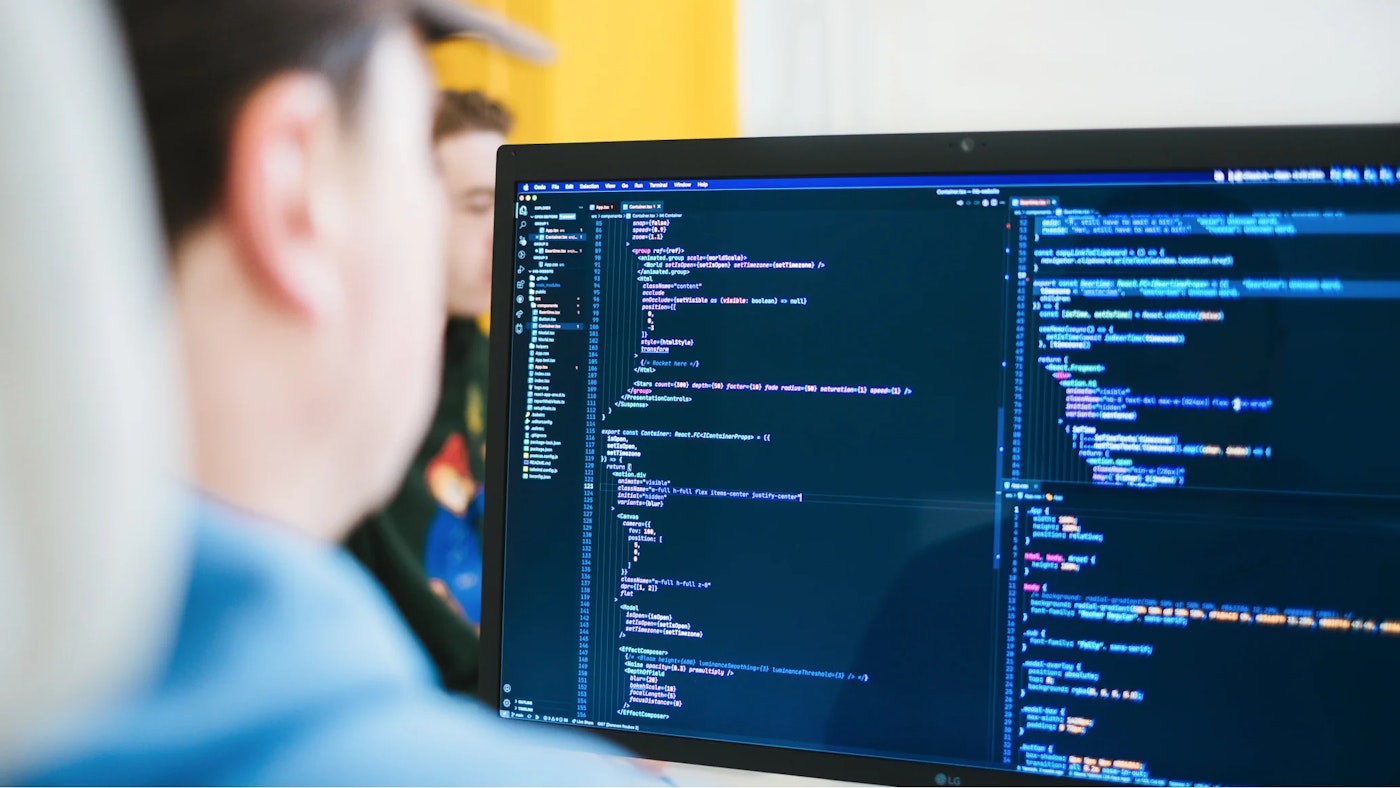 Monitor showing a code editor with code. Out of focus on the right of the photo is the person who is writing the code.