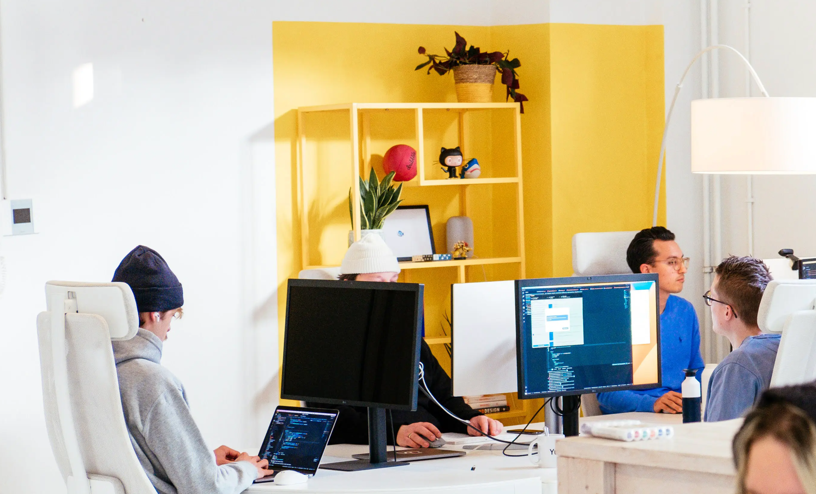 multiple designers and developers sitting at a desk looking at monitors while working