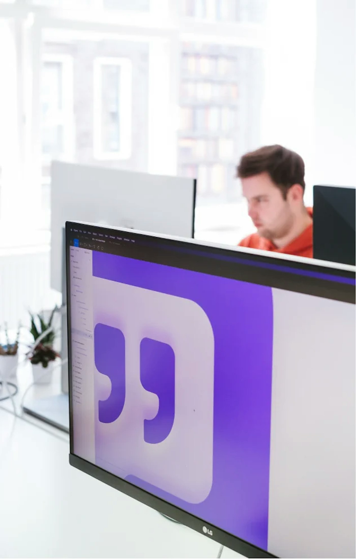 Monitor showing a larger purple themes icon design. In the rear is a person working behind their computer.