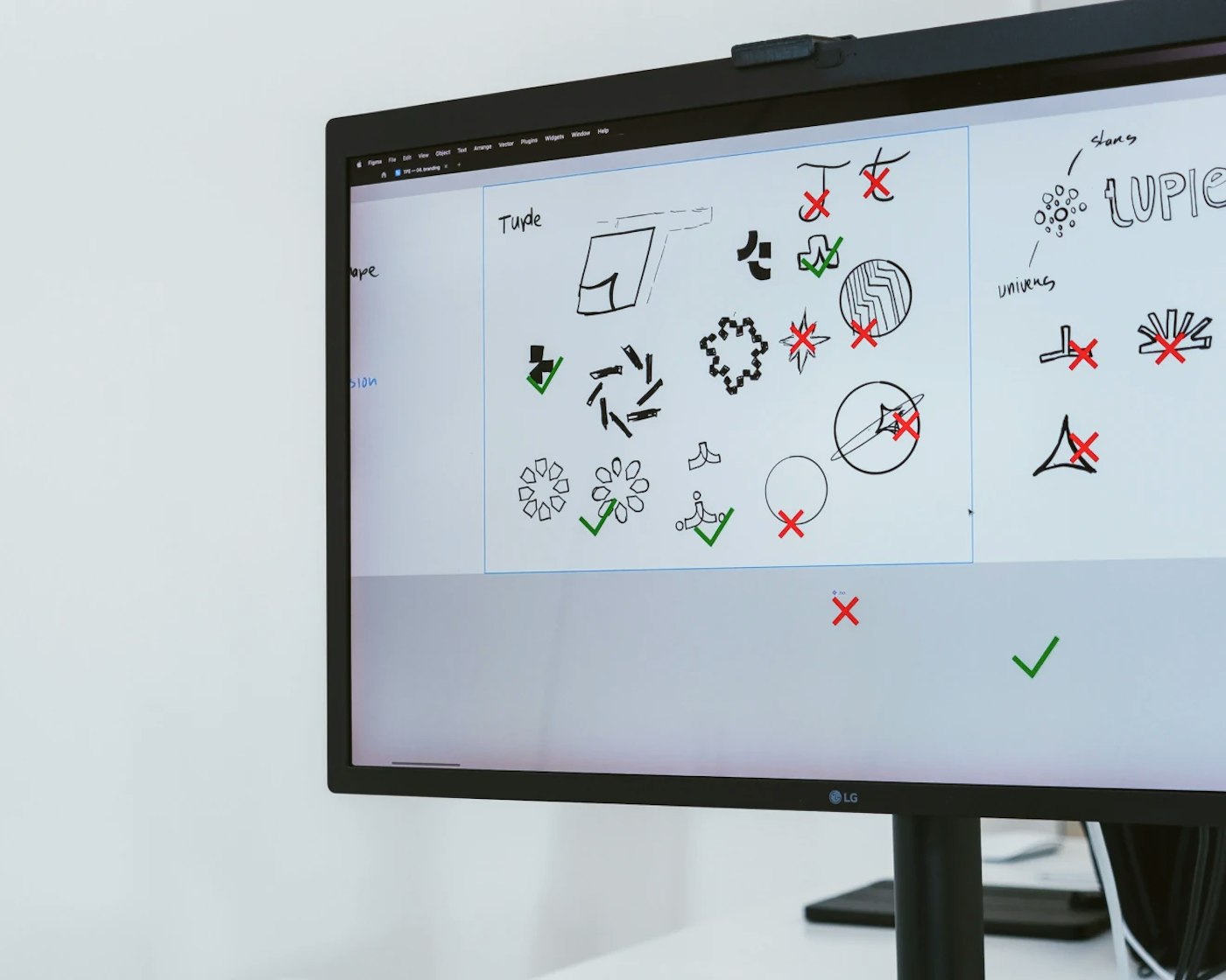 Computer monitor showing logo concept sketches with green checkmarks and red crosses.