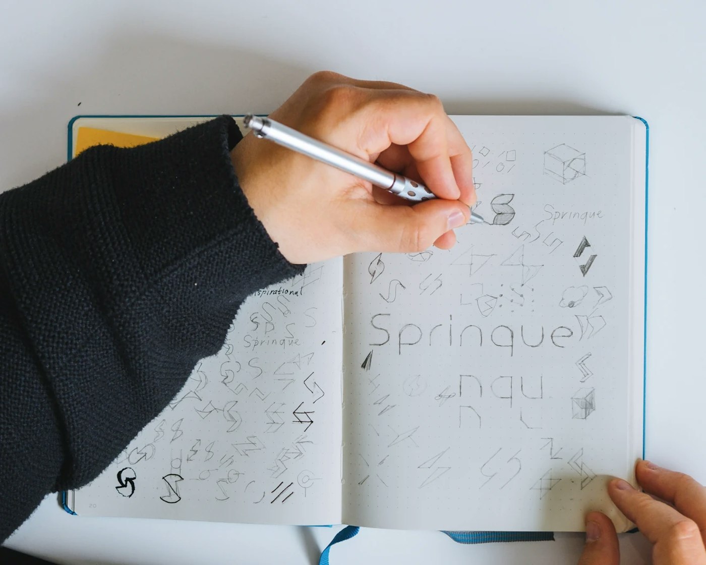 Hand drawing logo sketches in a grid note book with a pencil.