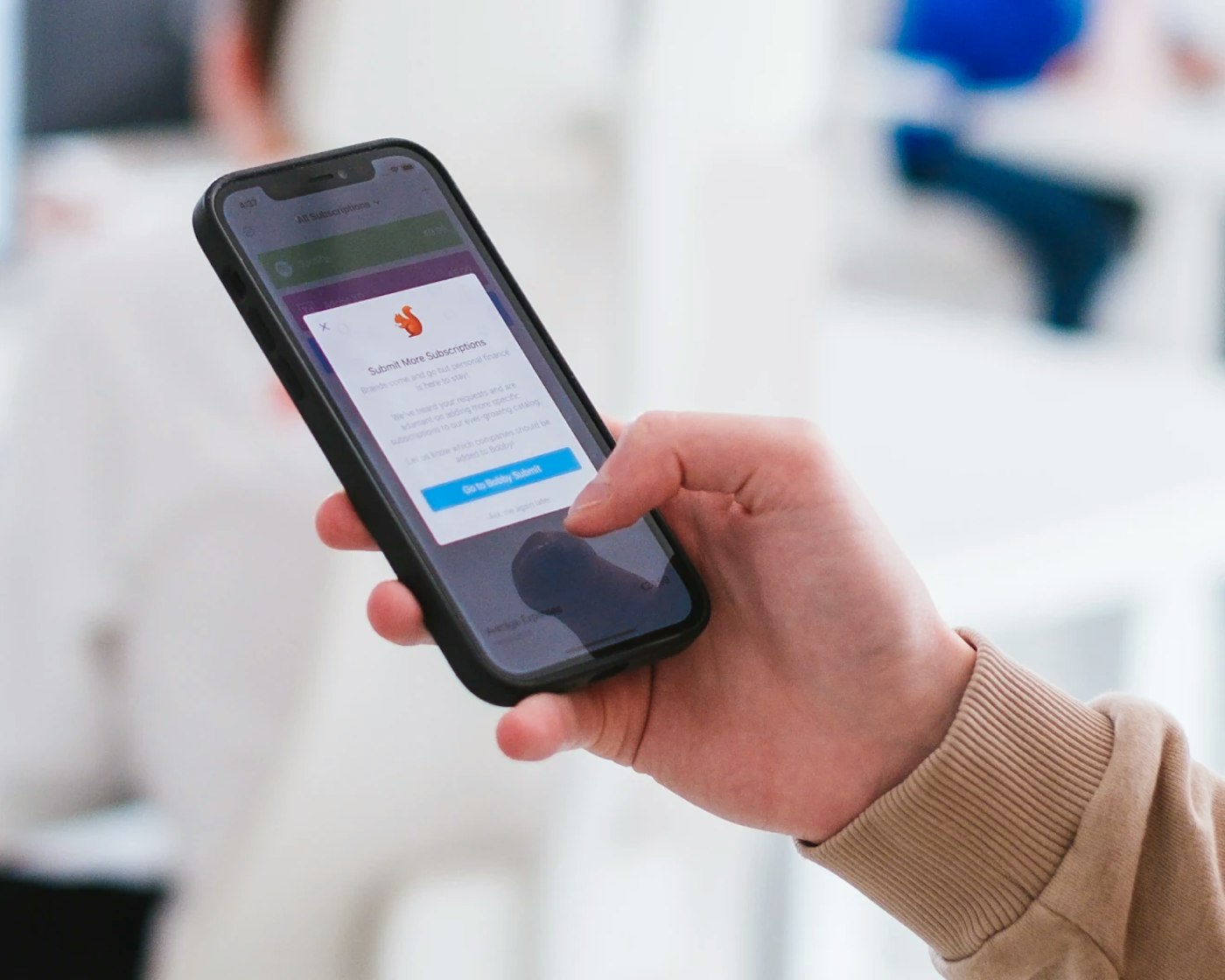 Hand holding a smart phone that shows  a white popup window with an orange logo, a paragraph of text and a bright blue button.