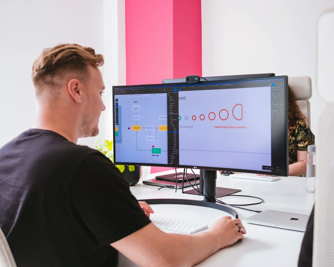 Person in a white interior office looking at a user interface on their computer monitor. In the background is a pink colored pillar.