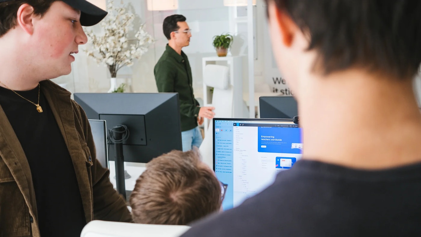 Person as seen from behind, looking at their computer monitor. The computer monitor shows a white window with blue cards. On the right is someone's neck and shoulder, out of focus.