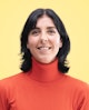 Portrait of person dressed in a bright red turtleneck sweater, against a yellow backdrop.