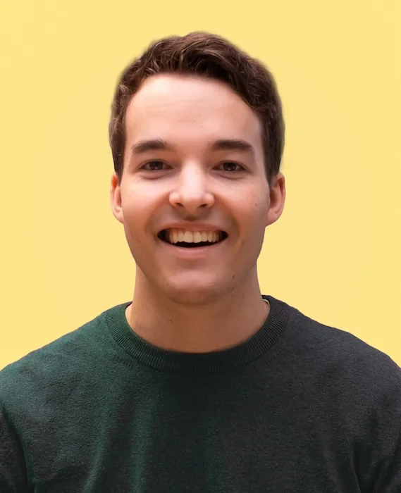 Portrait of person dressed in a dark green sweater, against a yellow backdrop.