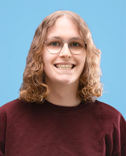 Portrait picture of Yummygum team member Evi, smiling, wearing a dark red sweater against a blue backdrop