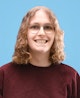 Portrait picture of Yummygum team member Evi, smiling, wearing a dark red sweater against a blue backdrop