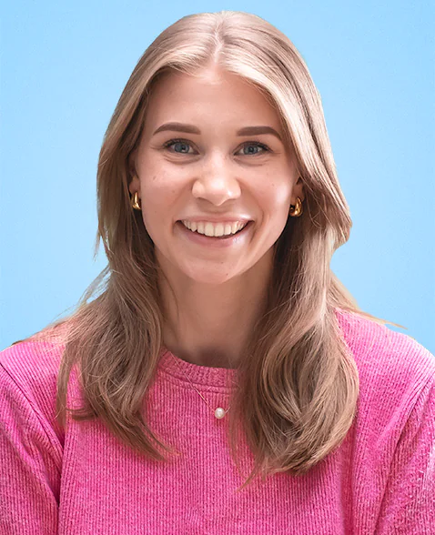 Portrait of Yummygum team member Megan, wearing a pink sweater in front of a light blue backdrop.