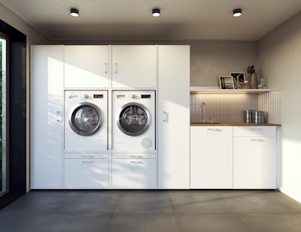 Waschküche mit weißem Waschmaschinenschrank mit schmalen Hochschränken und Waschbecken rechts.