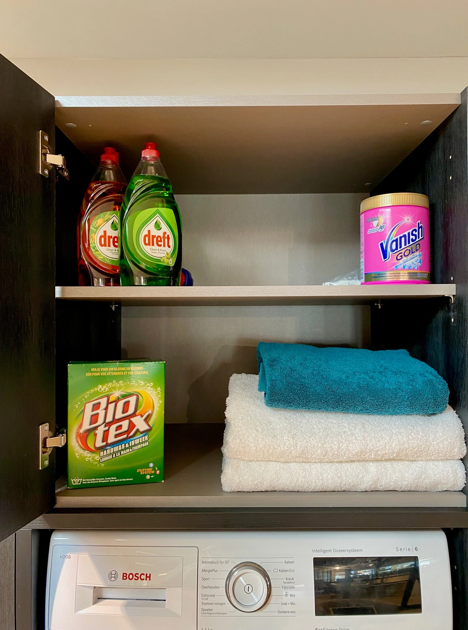 Lifestyle picture of top cupboard open showing cleaning detergents and towels