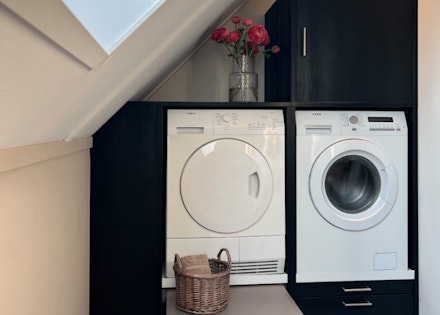 Idee voor wasmachine en droger op zolder: wasmachine kast met uitschuifplateau voor wasmand onder schuin dak