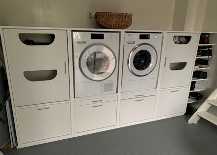 Voorbeeld hoe een waskamer ingericht kan worden in een kleine ruimte met een witte wasmachine kast en opbergruimte voor je wasmand