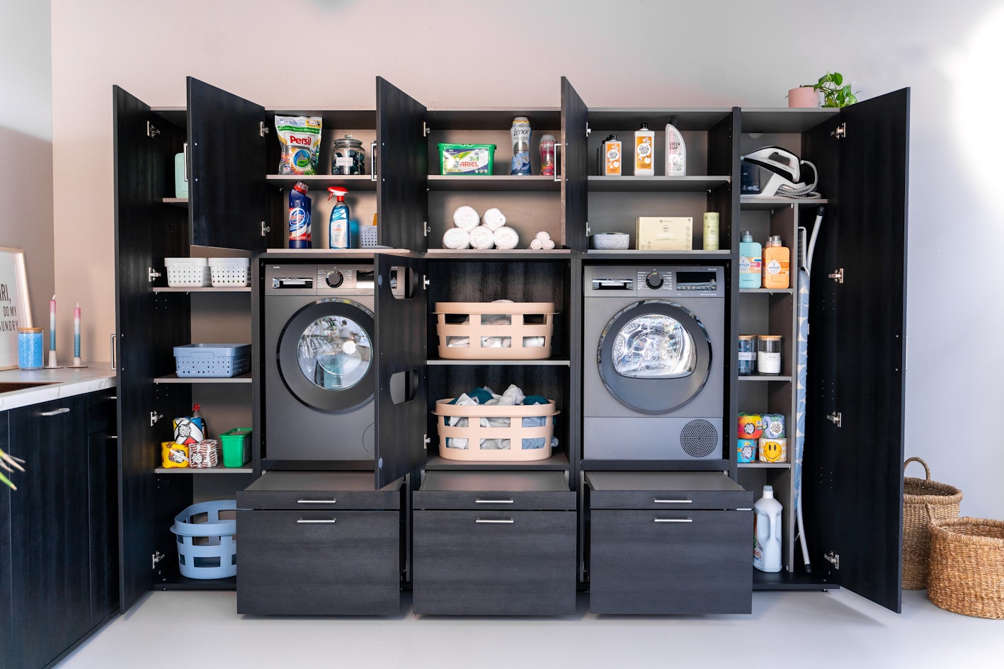 wasmachine kast zwart opbergkasten met wasbenodigdheden en deuren en wasmachine en droger naast elkaar
