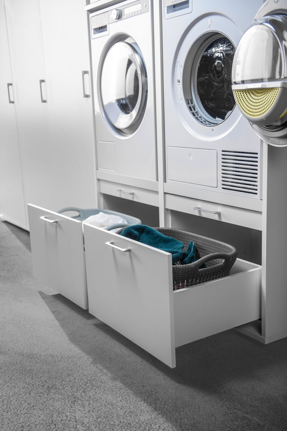 Dubbele wasmachine kast met droger en wasmachine naast elkaar met korflade voor wasmand en wasproducten en uittrekplateau in het wit in de wasruimte verhoger inspiratie ideeen