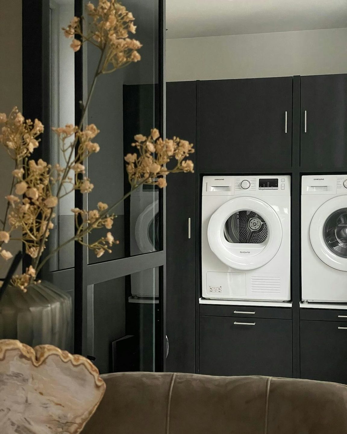 dubbele wasmachine kast zwart naast elkaar wasmachine en droger woonkamer inspirate ideeen met bovenkasten en uittrekplateau en korflade voor wasmand met decoratie