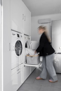 Ein Hauswirtschaftsraum mit weißem Schrank für Waschmaschine und Trockner nebeneinander. Waschturm Inspiration Ideen