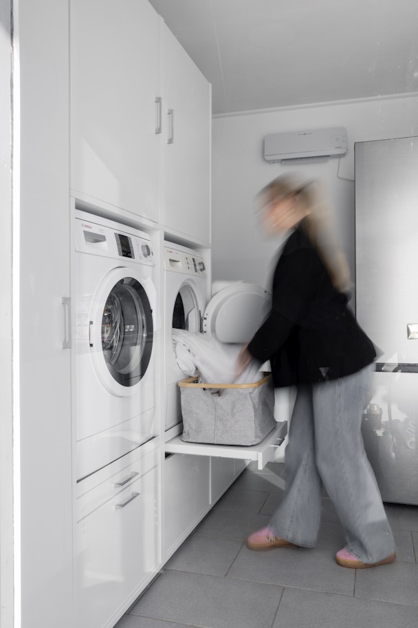 Ein Hauswirtschaftsraum mit weißem Schrank für Waschmaschine und Trockner nebeneinander. Waschturm Inspiration Ideen