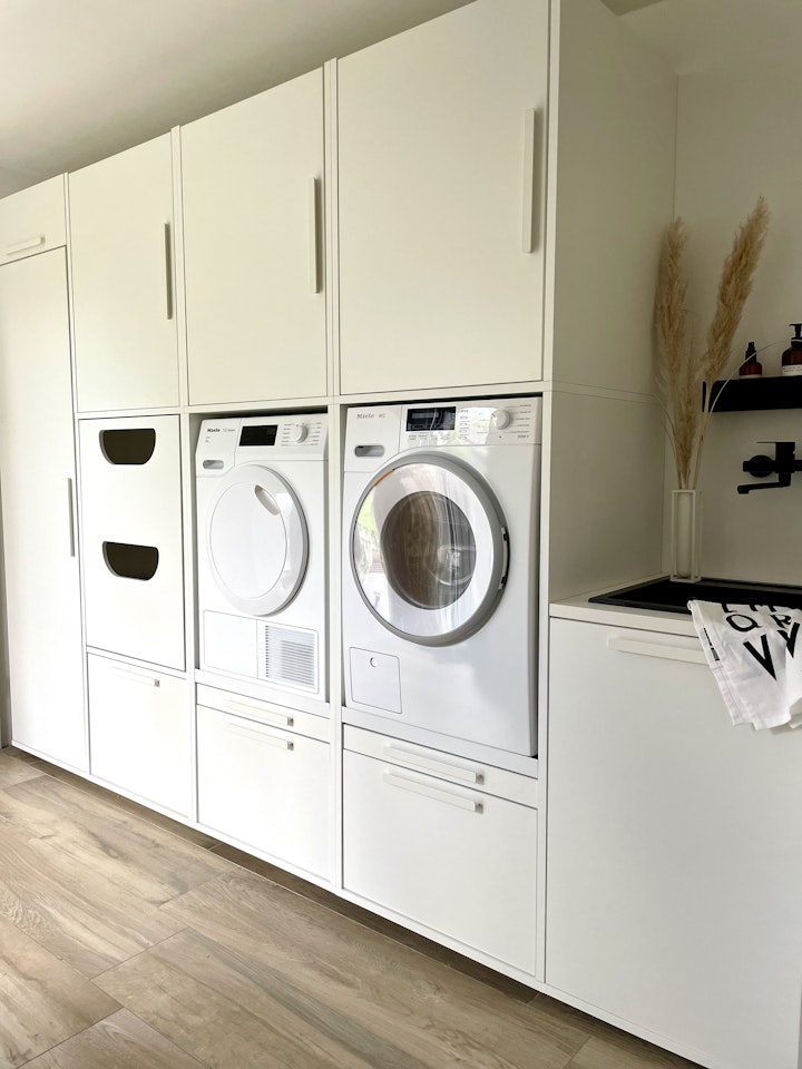 weißer Schrank für Waschmaschine und daneben Trockner und einem Unterschrank mit Spüle