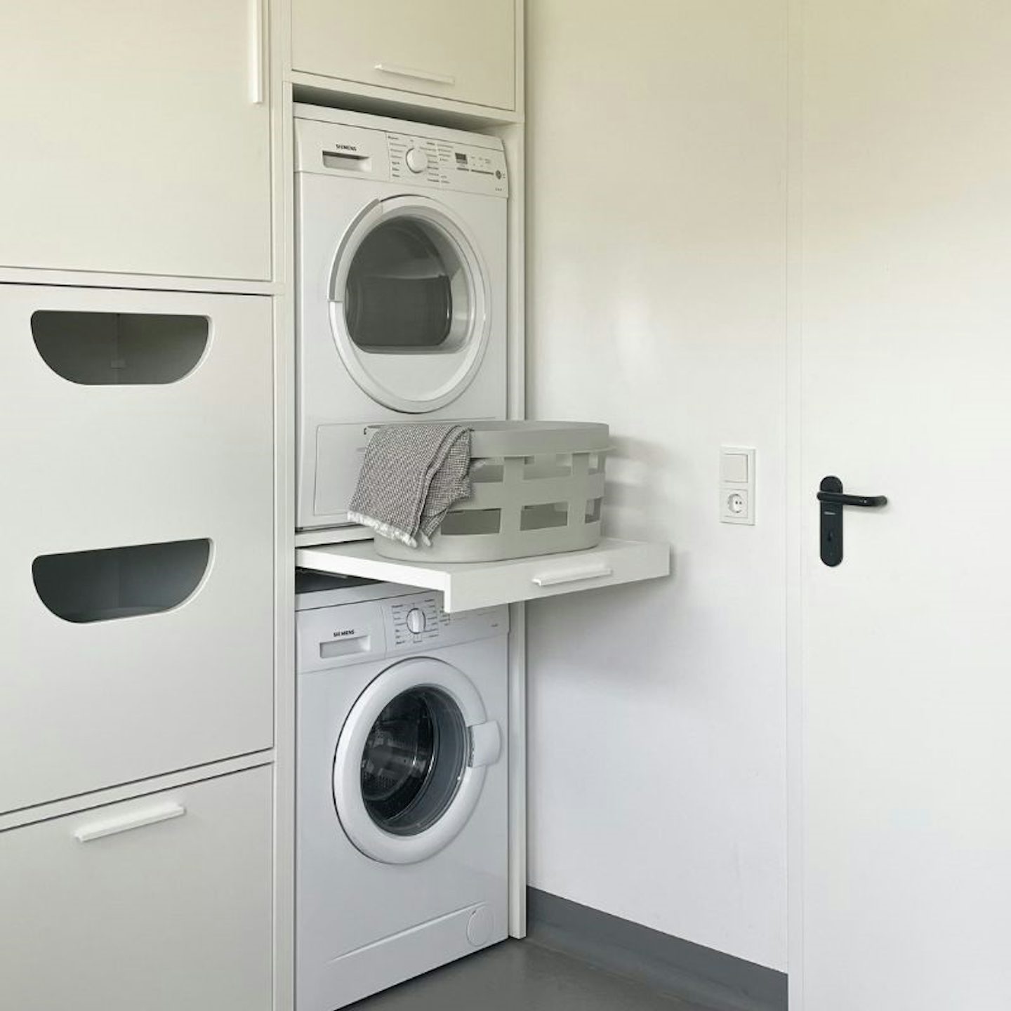 Ein weißer Hochschrank im Waschraum für Waschmaschine und Trockner übereinander. Waschturm Inspiration Ideen