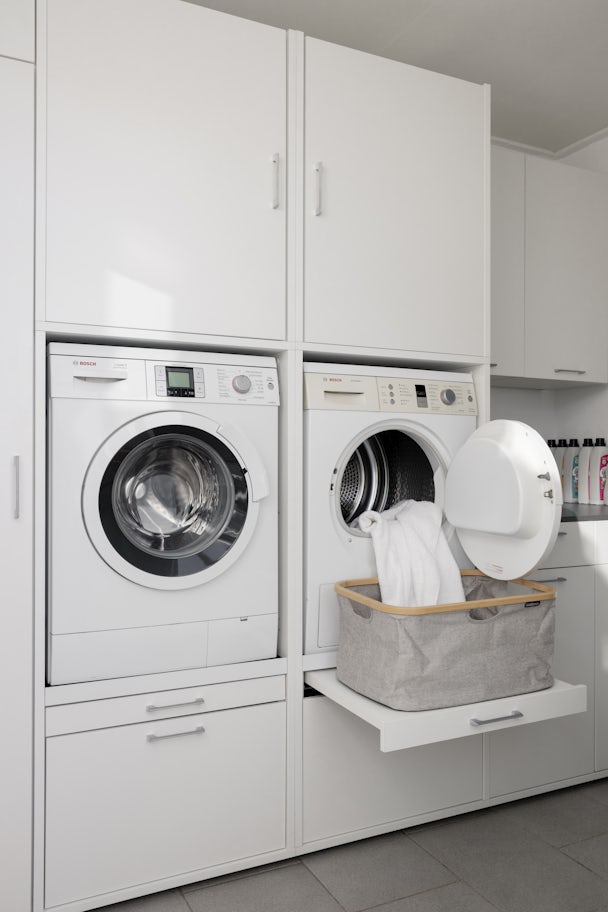 dubbele wasmachine onderkast wit met uittrekplateau voor wasmand met wasmachine en droogkast naast elkaar en opzetkast en onderkasten met keukenblad erop voor bijkeukenopstelling verhoger