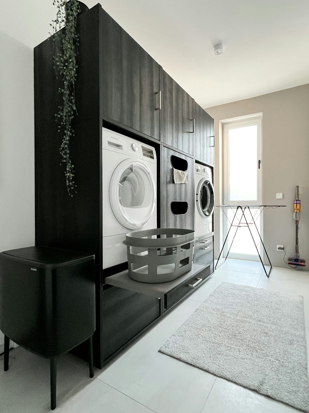 dubbele wasruimte kast zwart met wasmachine en droogkast naast elkaar met uittrekplateau voor wasmand interieur inspiratie ideeen voor wasplaats met verschillende opbergkasten voor wasproducten verhoger