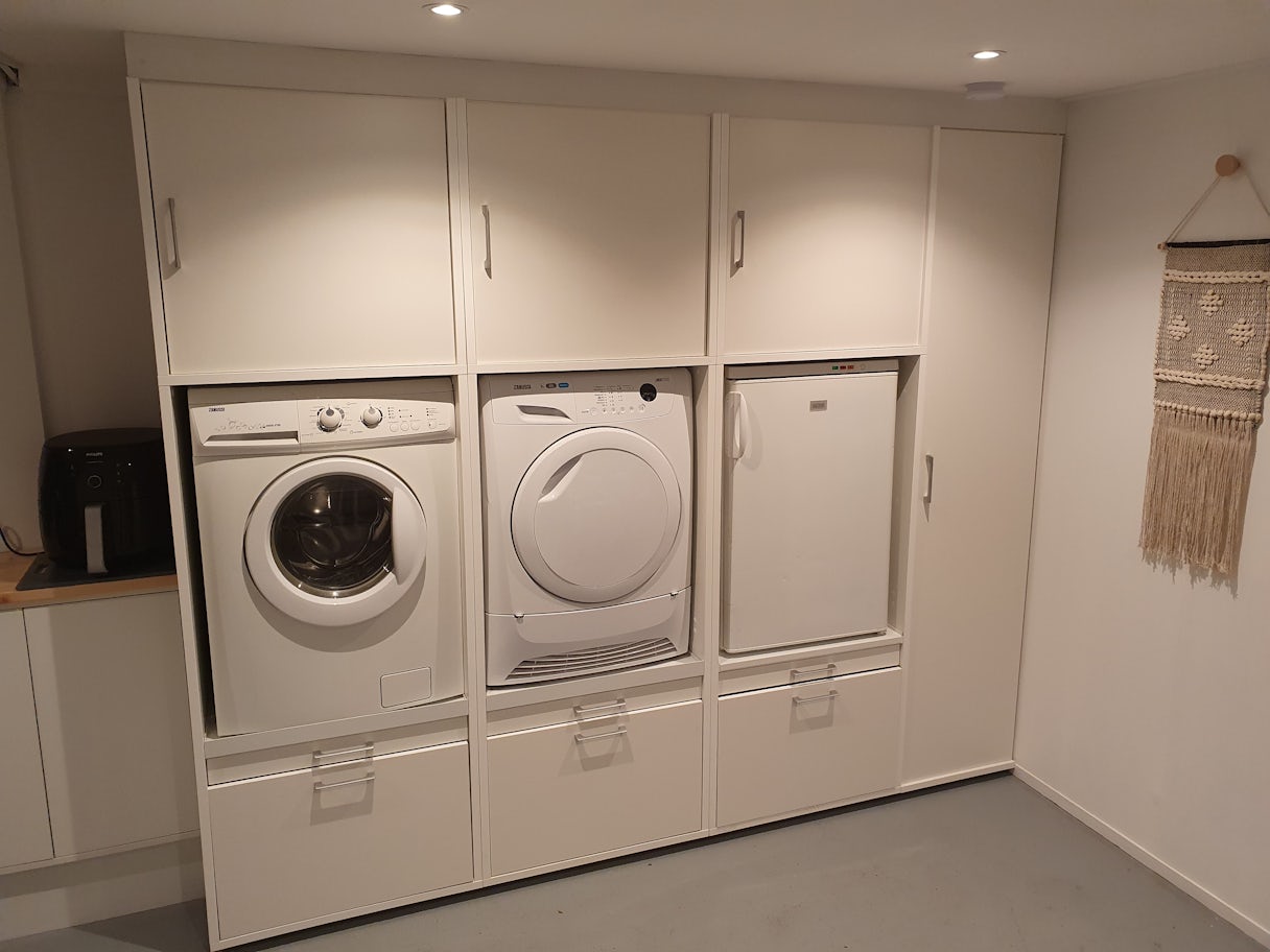 weißer Schrank für Waschmaschine und daneben Trockner und Kühlschrank