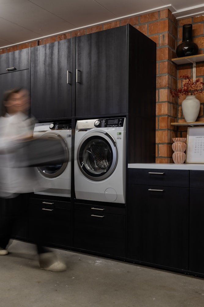 Wastoren Wasmachine opbergmeubel in het zwart met wasmachine en droger naast elkaar in de bijkeuken met verschillende opbergkasten