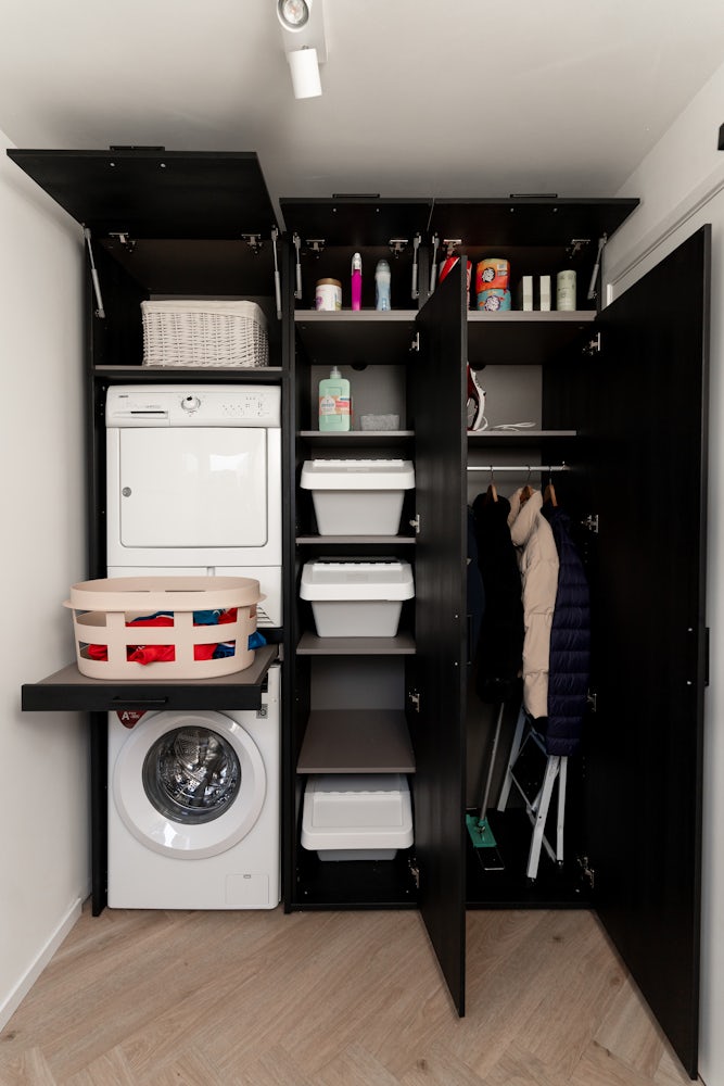 Wastoren wandkast zwart met wasmachine en droger op elkaar met uittrekplateau voor wasmand en verschillende opgbergkasten