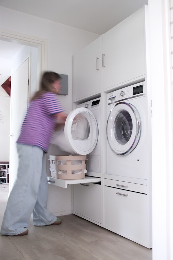 Wastoren dubbele wasmachine droogkast kast met een handig uittrekplateau voor de wasmand in het wit en andere verschillende opbergkasten met de wasmachine en droogkast naast elkaar verhoogd naar 60 centimeter waardoor je nooit meer hoeft te bukken.