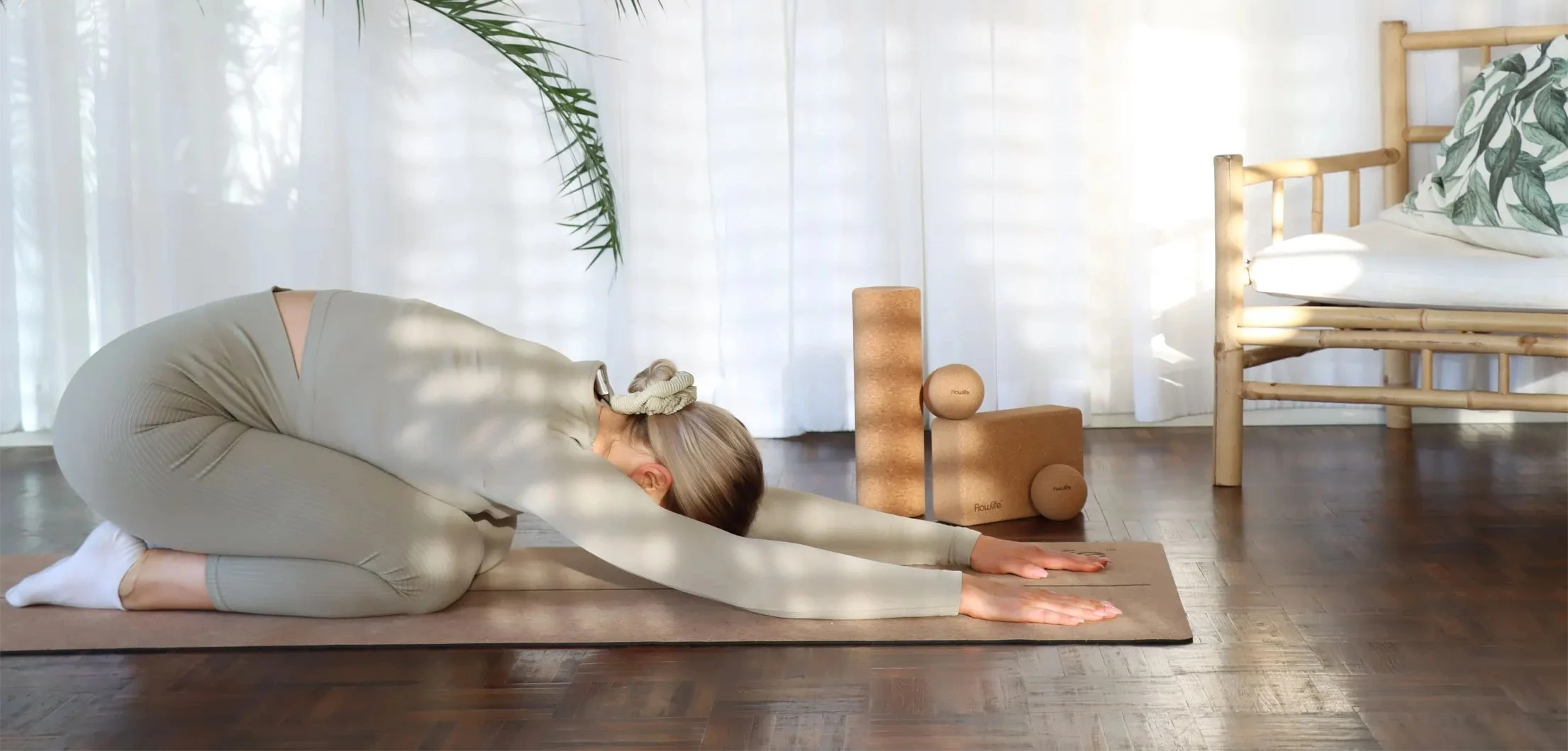 girl lying on a yoga mat in the yoga position child's position, in the background you can also see a roller, pressure ball and yoga blocks from Flowlife