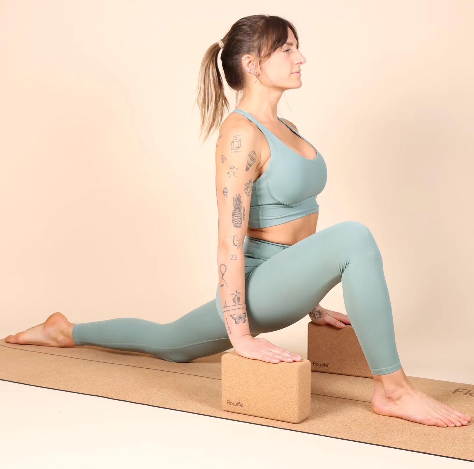  woman standing on a yoga mat in the yoga position low lunge where she holds her hands on a yoga block each to keep her balance better