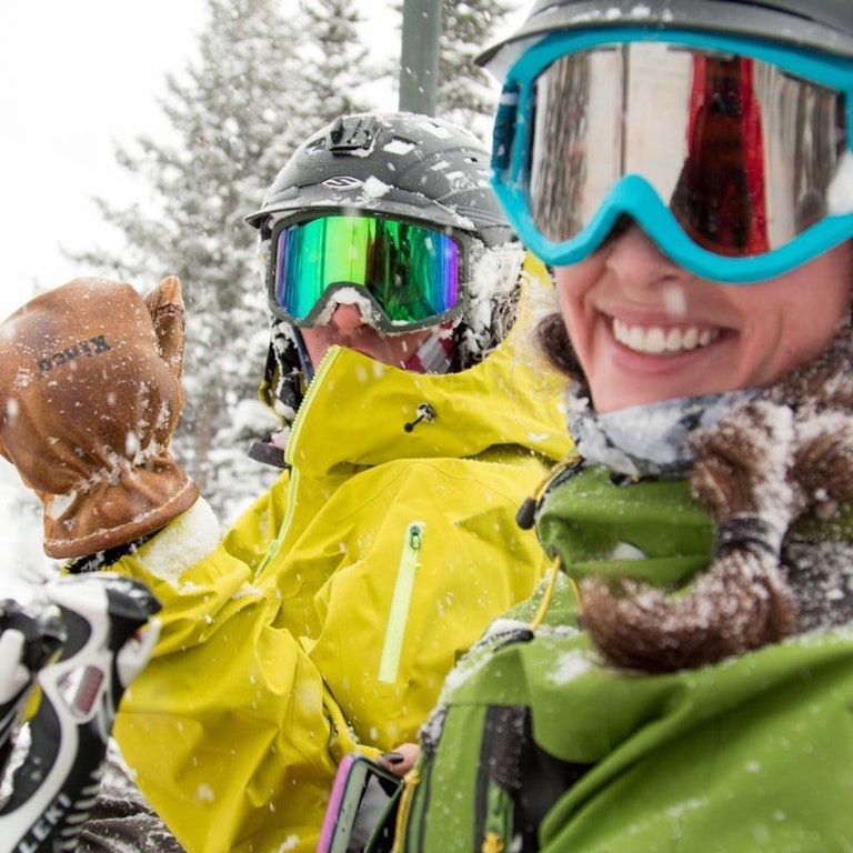 Two people smiling covered in snow on the chairlift
